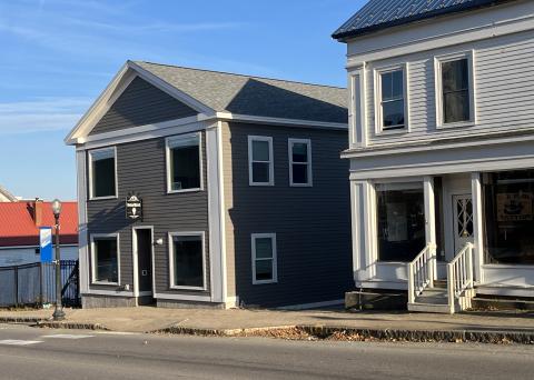 Two buildings are shown in the setting sun near a street and sidewalk. Both buildings are two stories tall in a traditional New England design. The one on the left has a sign that says, "MaineStreet Business Building."