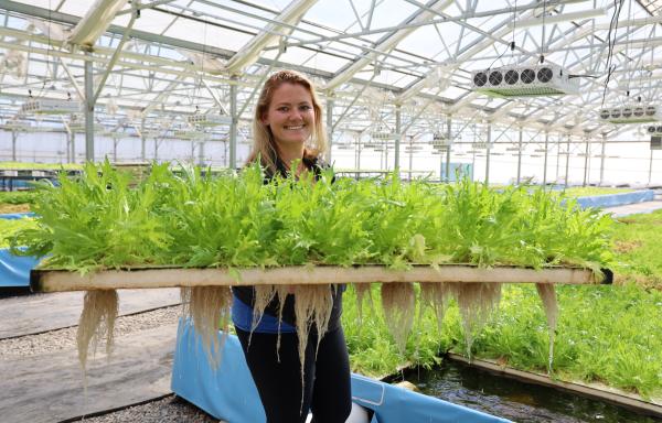 Woman holding lettuce grown in aquaponic greenhouse.