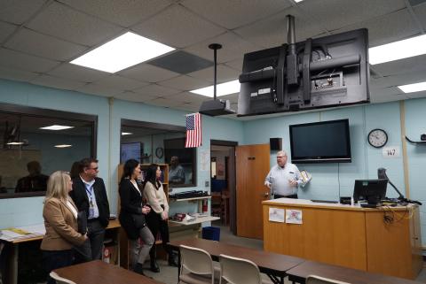 A group of people in a distance learning classroom. Televisions are hanging from the ceiling. 