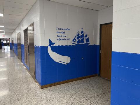 A school hallway shows a mural painted in bright blue and white with a whale and ship on it.