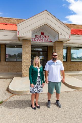 A woman and a man stand outside a building, which is labeled with the words "Dove Creek Town Hall."