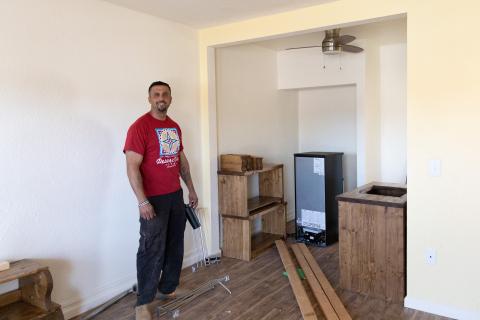 man standing in unfinished room with wooden furniture