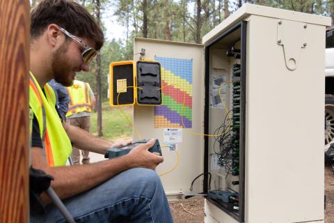 man holding equipment looking in fiber cable box