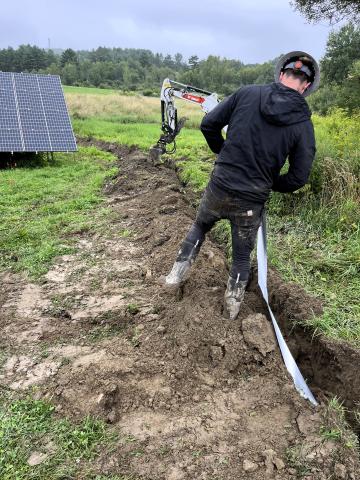 A solar installer is shown digging a trench through a grassy area at Junction Garden.