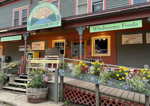 The front of the Marsh River Cooperative has various colorful signs, decorations, and blooming plants in season.