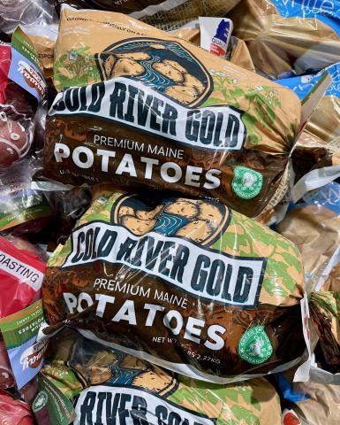 Bags of Cold River Gold Potatoes are shown stacked on a grocery store table.