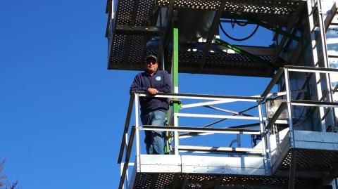 Pitreau stands on a landing of the grain dryer, silhouetted against a bright blue sky.