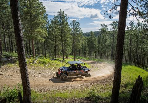An ATV is shown on a dirt trail in northern Maine with trees in the background and a blue sky overhead.