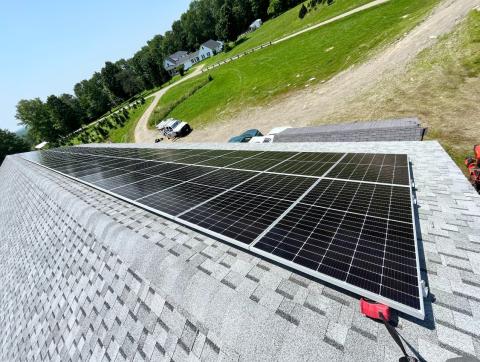 The solar array on the roof of the Piper Mountain barn is seen from the rooftop looking down at the yard with the house in the distant background.