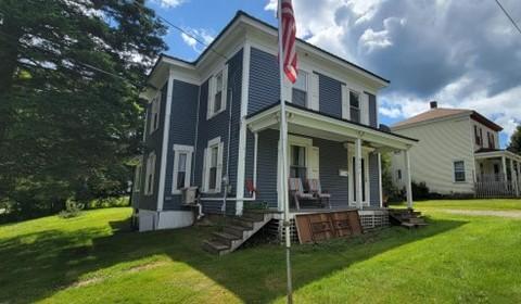 A two story grey home is pictured with a green lawn, bright blue sky, and trees in the background.