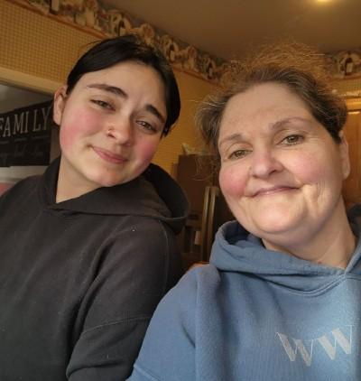 A woman and her daughter smile for a selfie portrait indoors. 