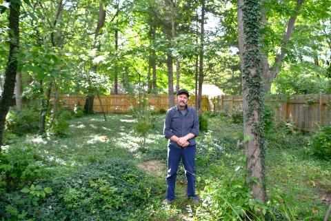 Man standing in wooded backyard of his house.