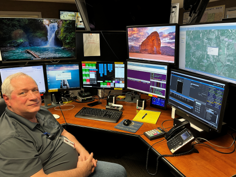 Man sitting at desk in front of multiple computer screens.