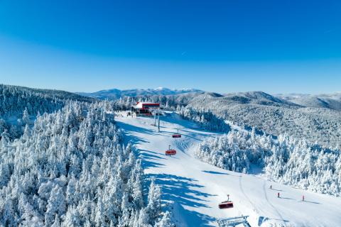 The image shows an aerial view of a ski lift with snow on the ground and a blue sky. It is the Jordan 8 lift at the Sunday River Resort in Maine.