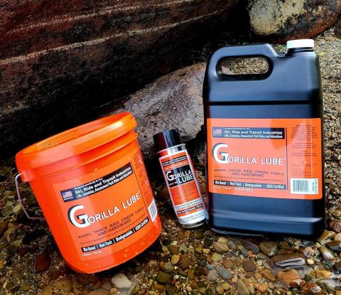 The photo shows three containers of Gorilla Lube, an industrial lubricant. The labels are bright orange, and the bucket, spray can, and jug are set on granite outdoors. 