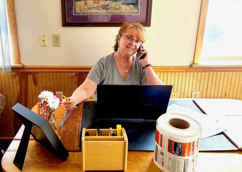 A woman sits at a desk in a sunny office.