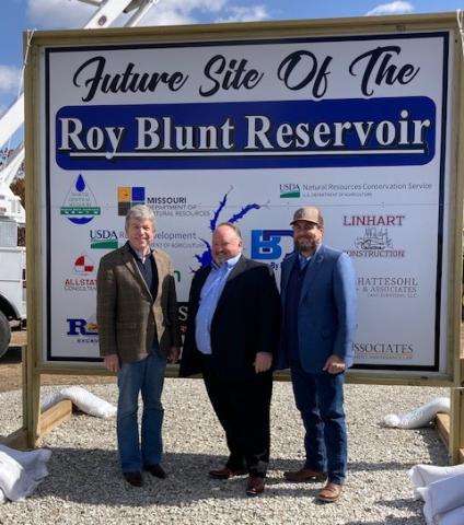 A photo of Missouri Rural Development State Director and representatives from North Central Missouri Rural Water Commission standing in front of a construction sign on the future site of the Roy Blunt Reservoir.