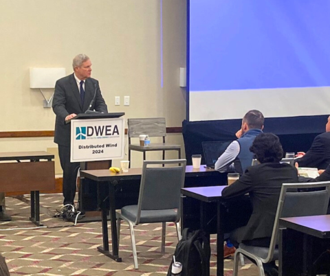 USDA Secretary Tom Vilsack addresses an audience in a conference room at a podium labeled with the Distributed Wind Energy Association logo. 