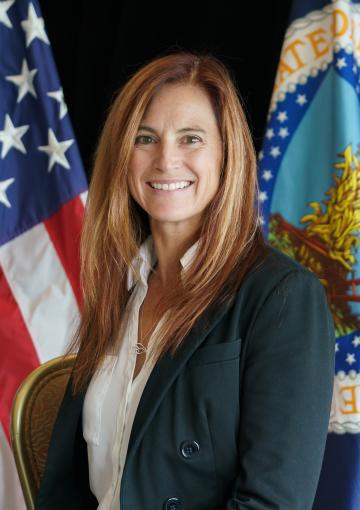 Utah State Director Michele Weaver, light skin female, with straight auburn, shoulder length hair, in front of American flag and Department of Agriculture flag.