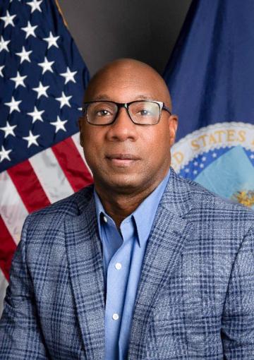 Clarence Bradley. a dark complexion male adult with bald head, wearing light blue collared dress shirt with  blue plaid blazer.