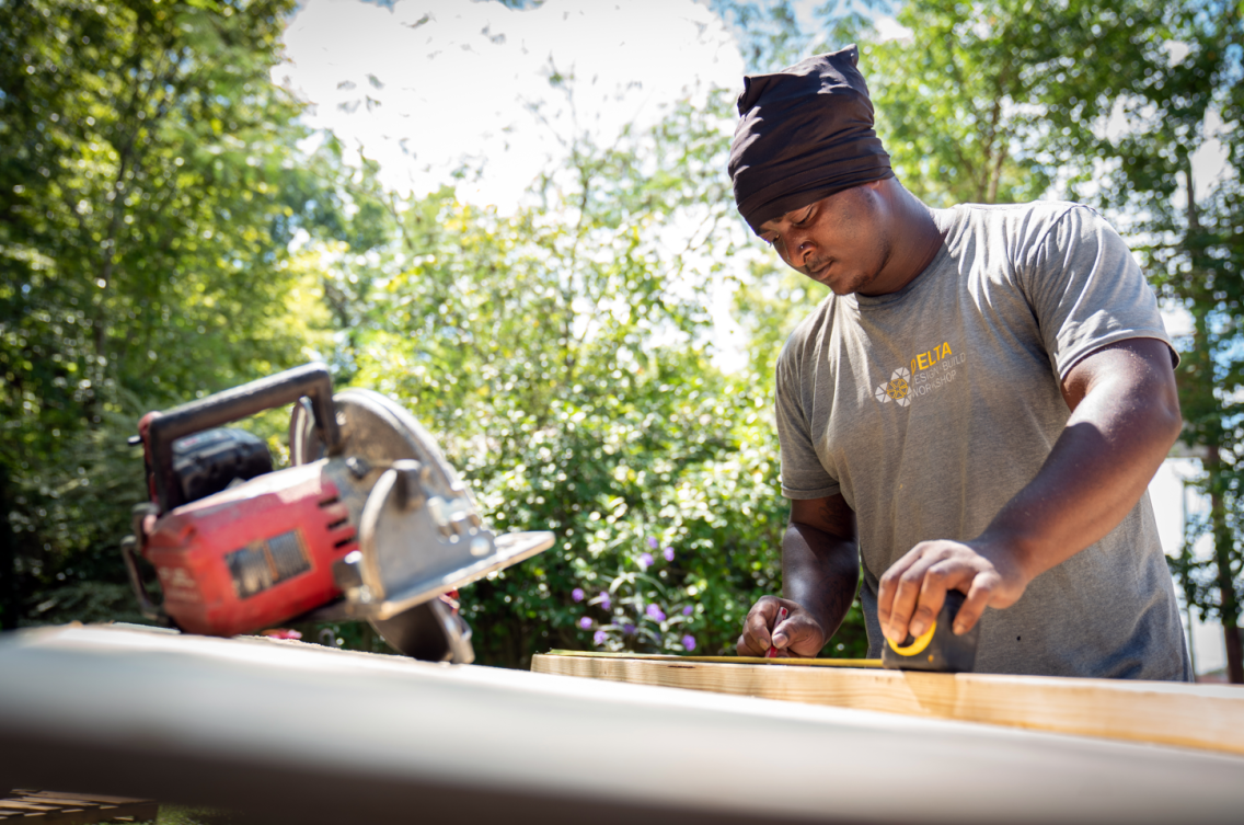 A man uses a measuring tape on a piece of wood next to a circular saw.