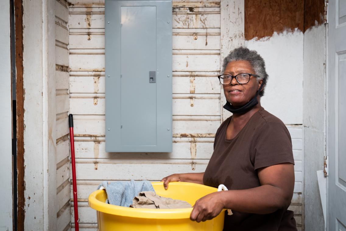 Woman holding a basket with clothes in it. She is standing in a room in front of a new electrical box.
