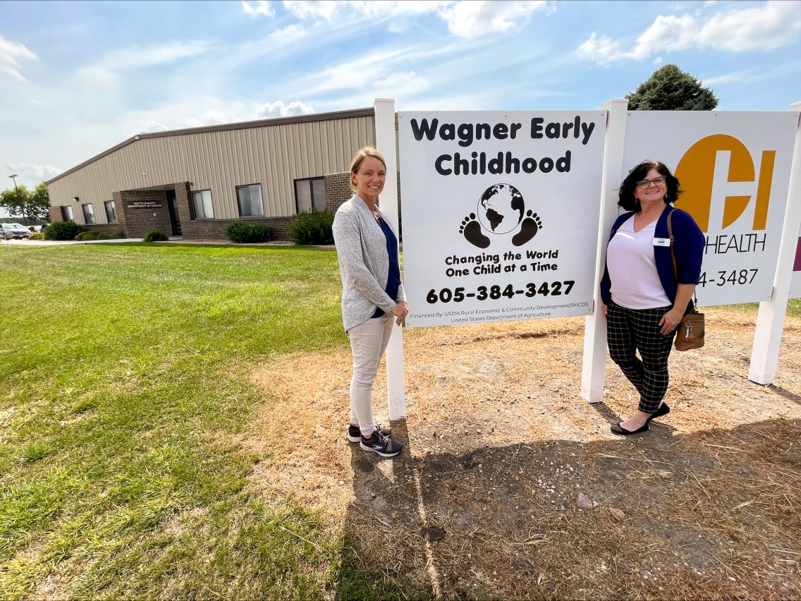 Rural Development State Director and Community Facilities Loan Specialist next to Wagner Early Childhood sign in front of their facility.