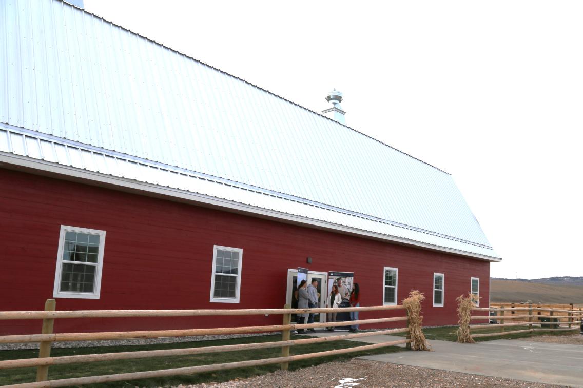 New long red barn owned by Rancher's Insurance with wooden ranch style fence in front of it.