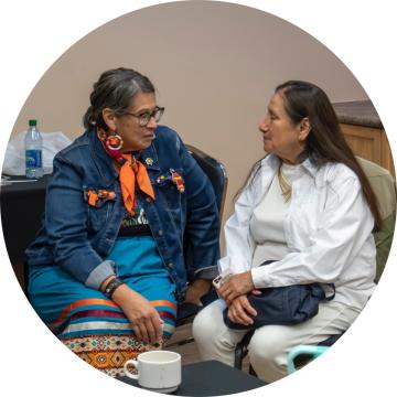 Native American ladies sitting in chairs, talking and smiling with each other.