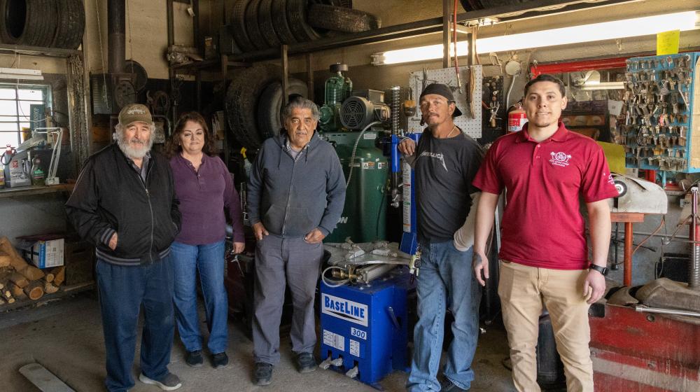 Five people pose for a photo in a tire shop garage area