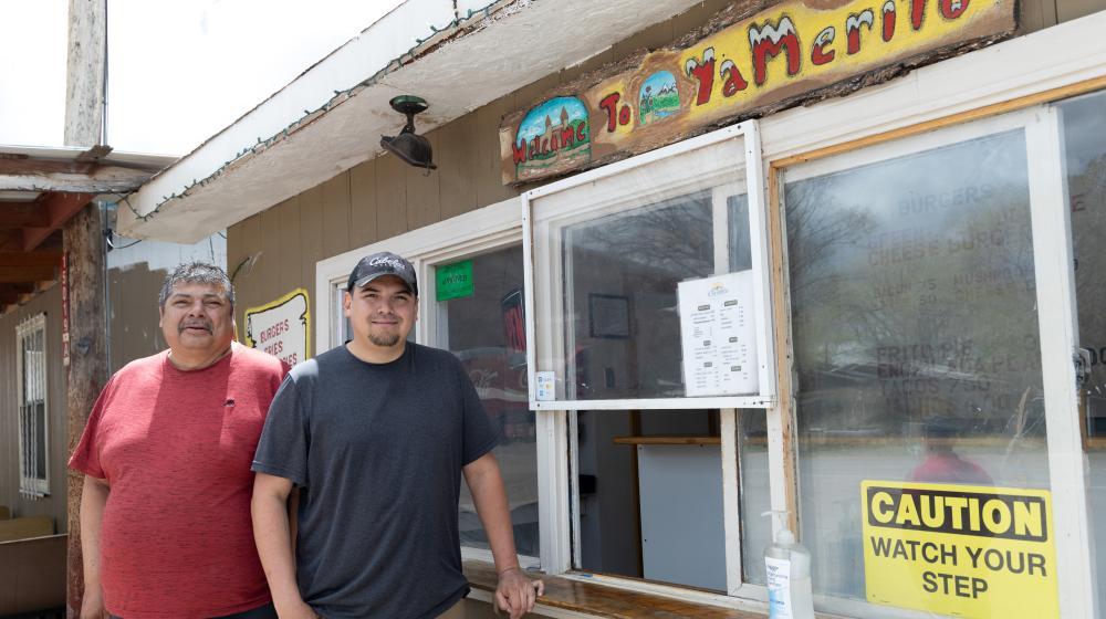 Two men stand to the left of an outside restaurant order window