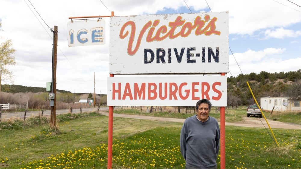 Man standing in front of Victor's Drive-In, Hamburgers sign