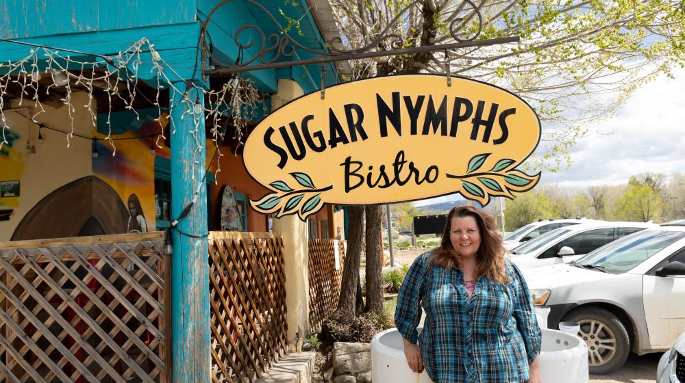 Woman standing under Sugar Nymphs Bistro sign next to parking lot