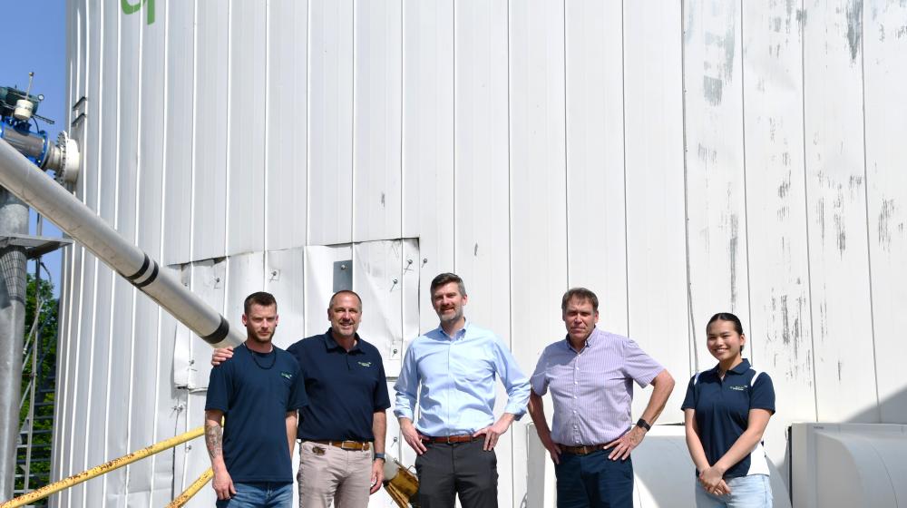 People standing in front of large bio-fertilizer storage tank.