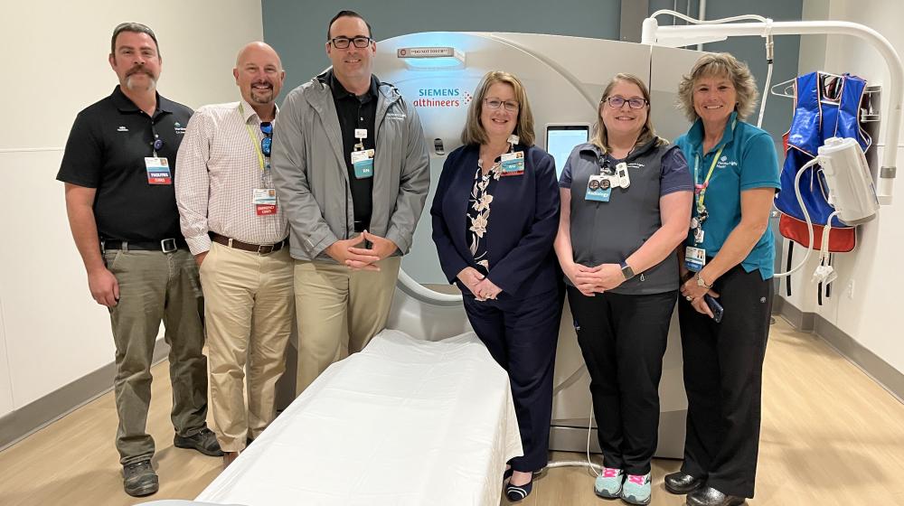 Three men and three women pose in front of a CT machine at CA Dean hospital. 