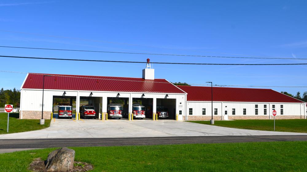 Rural fire station with trucks visible in five open bays. 