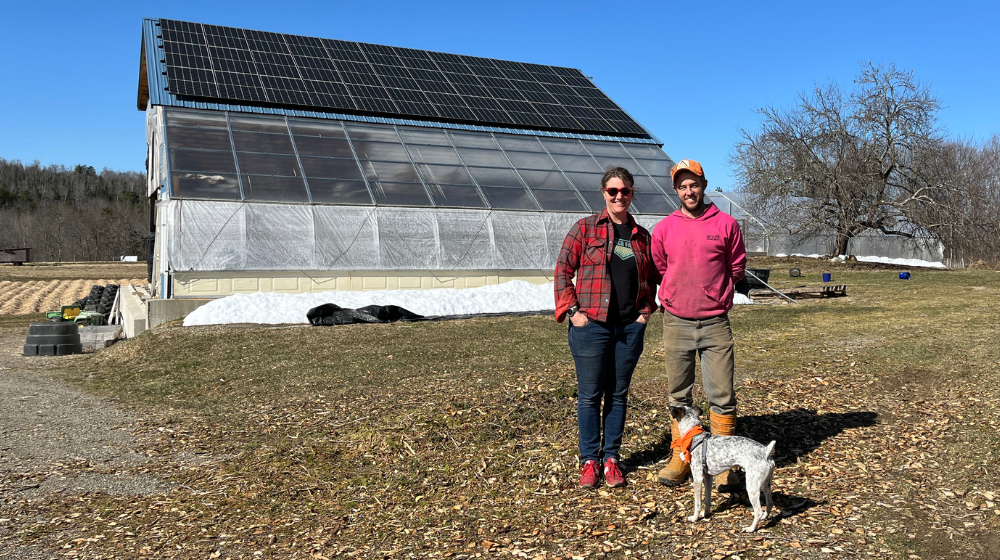 Molly and Everett pose with dog Cricket in front of their barn with the solar panels on the roof.