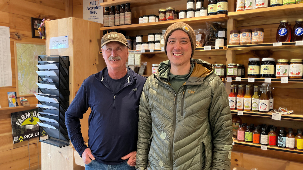 Owner Gary and manager Eric of Replenova Farm pose inside the farm store, with shelves of local foods arrayed behind them.