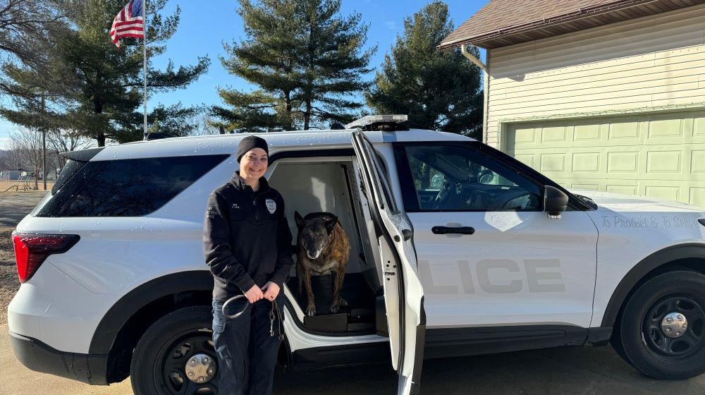 A police officer stands beside a police car with a police dog