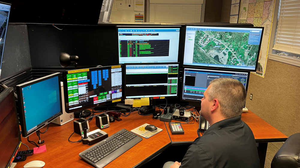 Man sitting at desk in front of many computer screens.