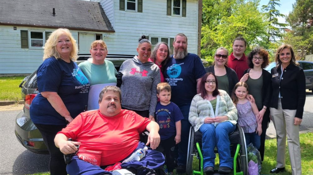 Family standing on the lawn in front of a white two-story house. Two family members are in wheelchairs.