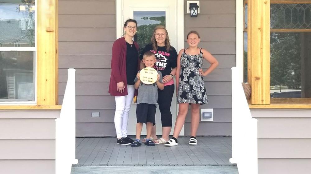 A USDA loan specialist stands on the steps of a house with the new homeowner and her family