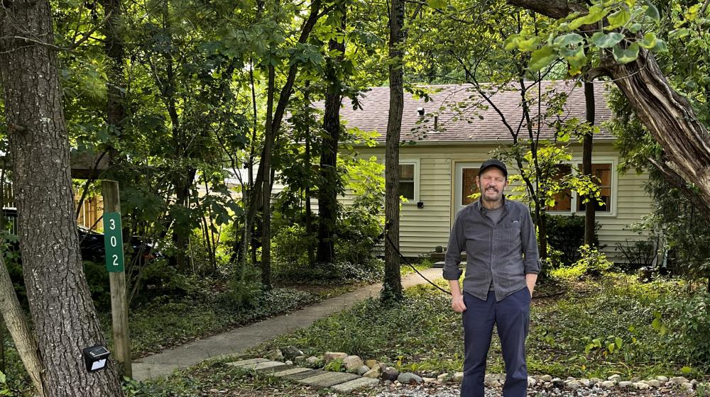 Man standing in front of house on wooded lot.