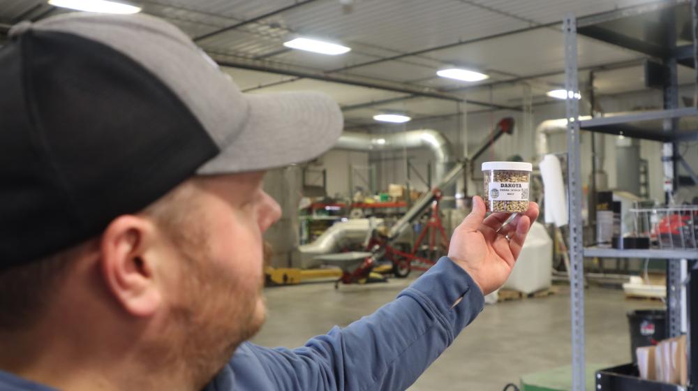 Jared Stober with an outstretched hand holding a small bottle with grains inside.