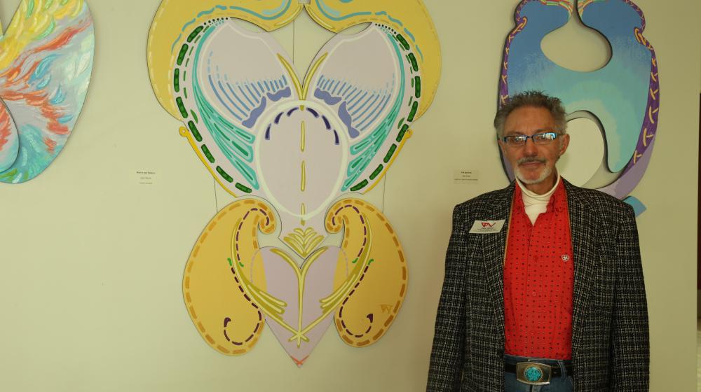 Artist John Welch standing in front of his colorful art in an exhibit.