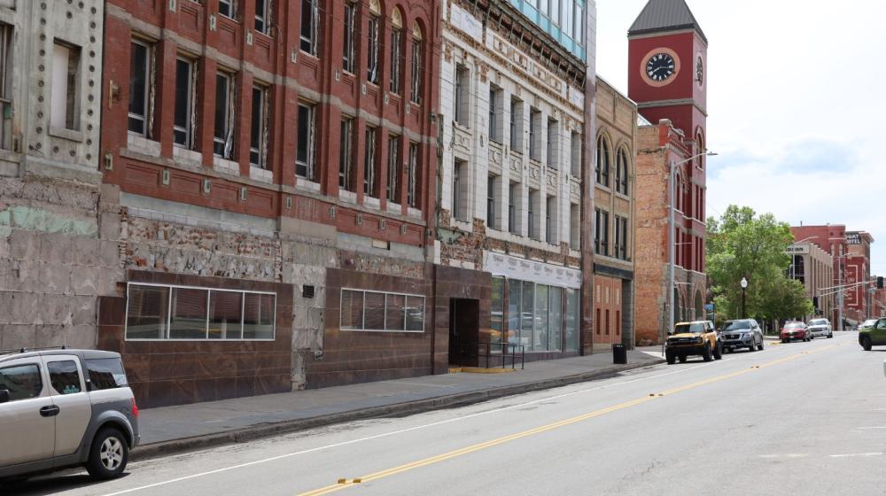 Brick buildings with many windows line a street in Montana. A clock tower is seen in the background.