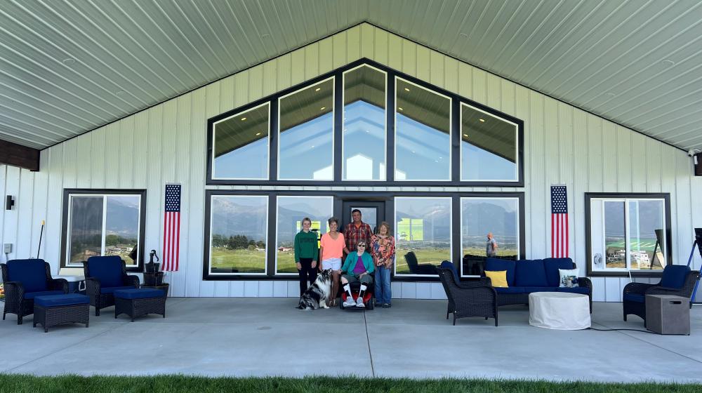 A group of residents stands outside a senior center on a cement patio. Large picture windows are behind them.