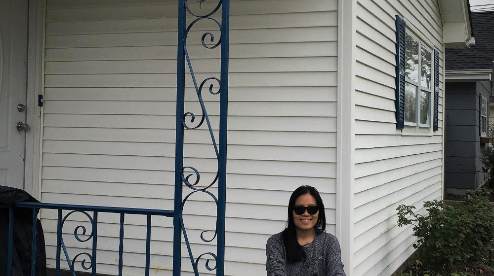 Smiling woman sitting on the brick front steps of a while house.