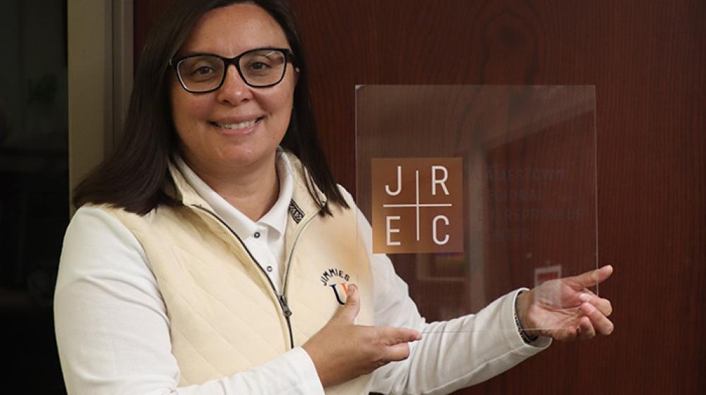 Katherine Roth, executive director of the Jamestown Regional Entrepreneur Center, holds a plaque with the letters "JREC" on it, the abbreviation for her organization.