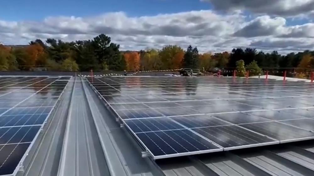A solar array on the top of a roof with fall colors in the trees behind